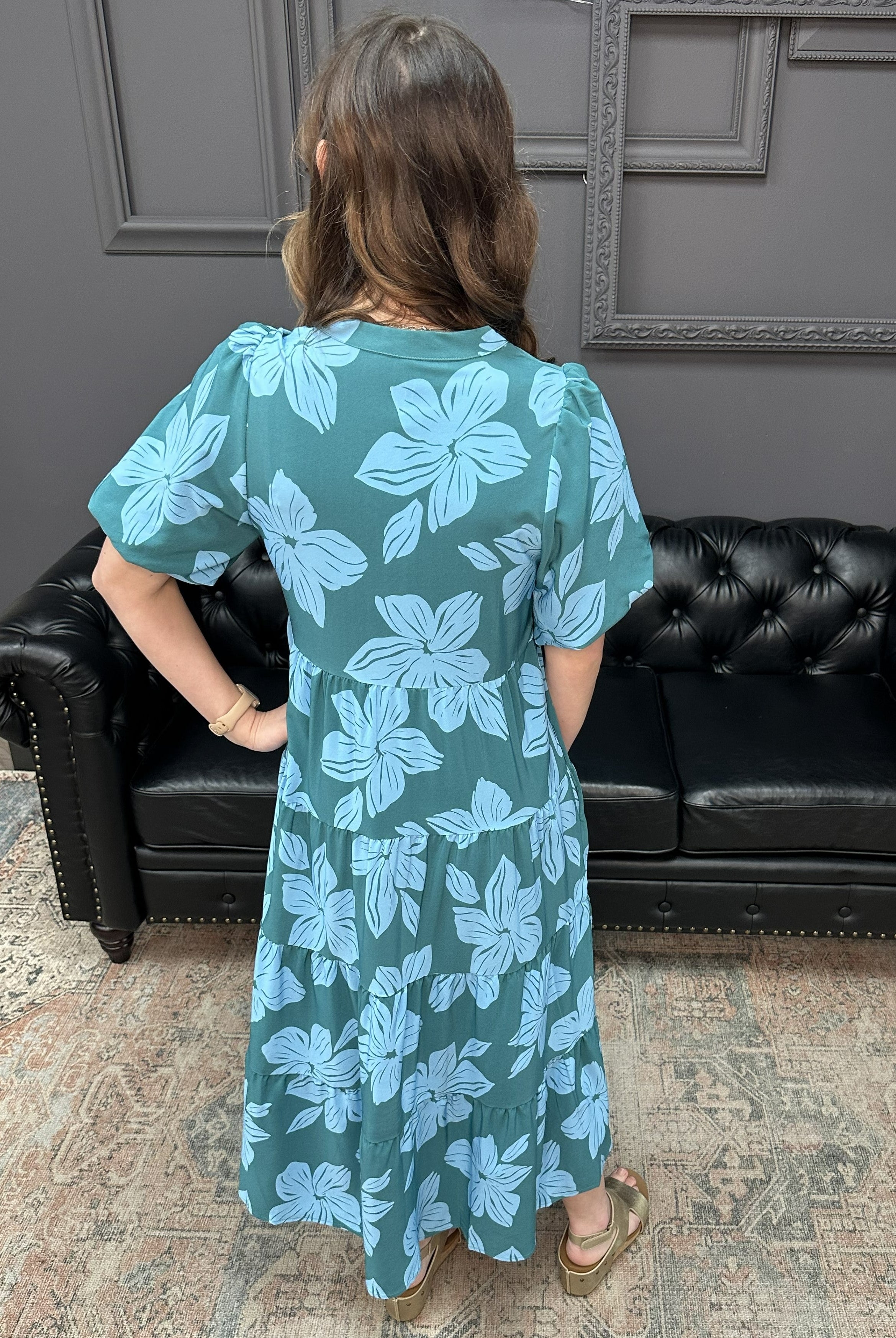 Woman wearing a green dress with blue floral pattern in a living room.