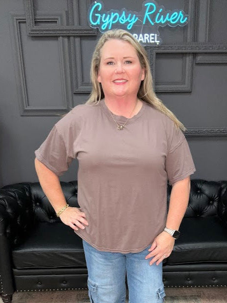Woman wearing a brown t-shirt and blue jeans standing in a room with a black couch and decorative items.
