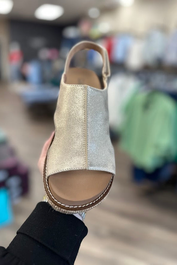 Gold glittery sandal held in front of a store with blurred background
