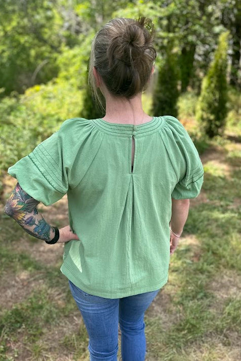 Person wearing a light green blouse with puffed sleeves in a forest setting