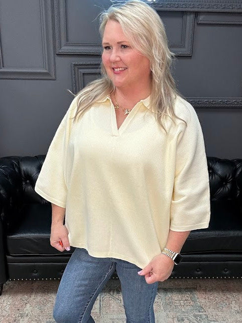 Woman wearing a light-colored blouse and blue jeans standing in a room with a black leather couch.