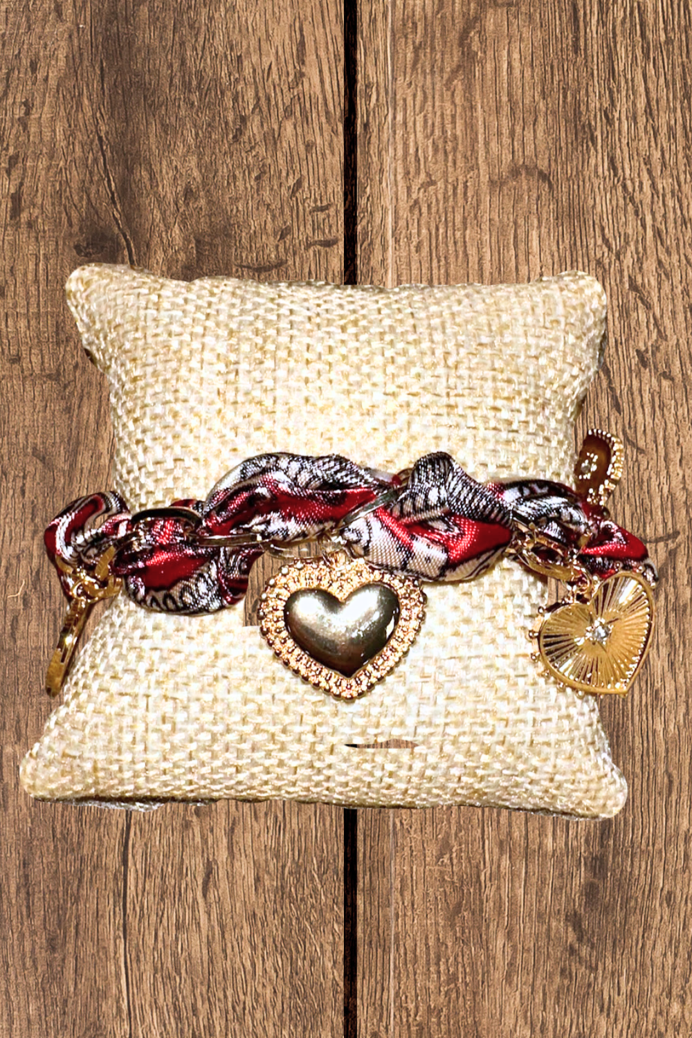 Multicolored braided bracelet with heart and circular charms on a decorative pillow against a wooden background