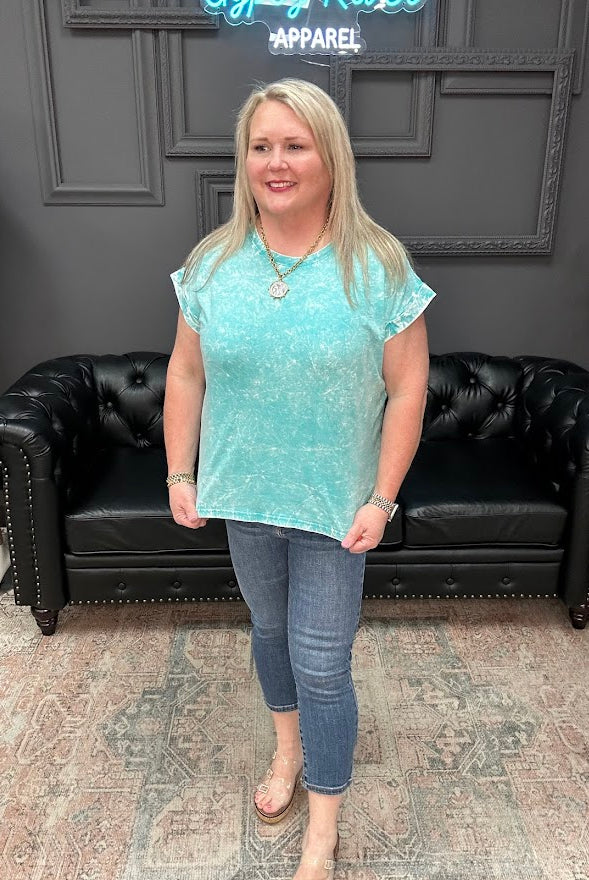Woman wearing a light blue top and jeans standing in a room with a black leather couch and gray walls.