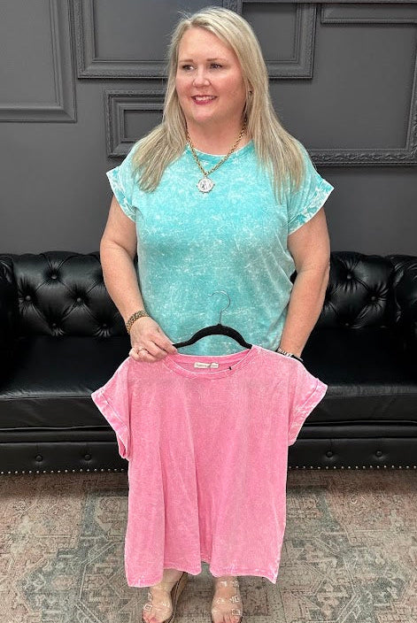 Woman holding a pink shirt in a store setting with a black leather couch and gray walls.