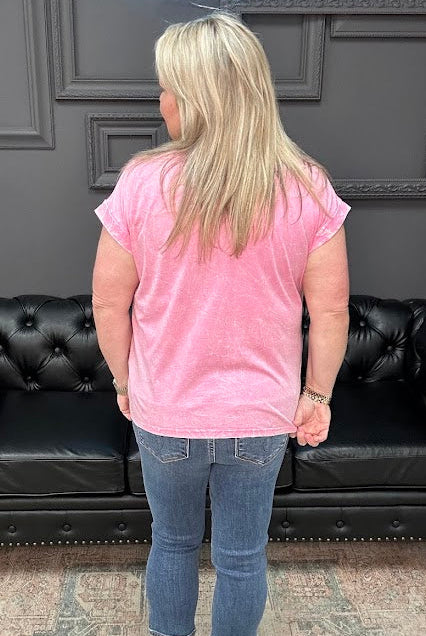 Person wearing a pink shirt and blue jeans standing in front of a black leather couch.