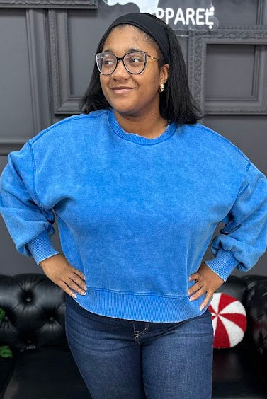 Woman wearing a blue sweatshirt and jeans standing in a living room with a Christmas tree and decorations.