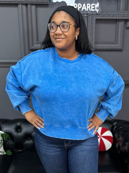 Woman wearing a blue sweatshirt and jeans standing in a living room with a Christmas tree and decorations.