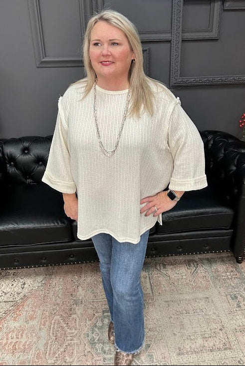 Woman wearing a white blouse and blue jeans standing in a room with a black leather couch and gray walls.