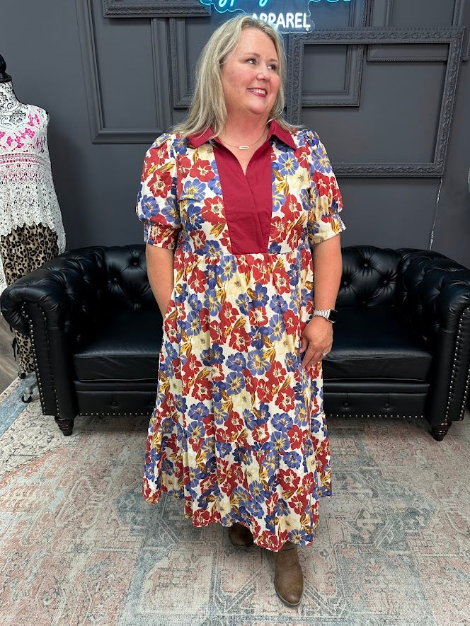 Woman wearing a floral maxi midi dress standing in a room with black leather chairs and a gray wall.
