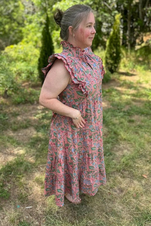 Woman in a floral dress standing outdoors with greenery in the background