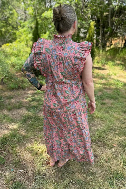 Person wearing a floral dress standing in a grassy outdoor area.