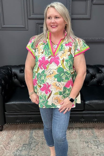 Woman wearing a colorful floral blouse and jeans standing in front of a black leather couch.