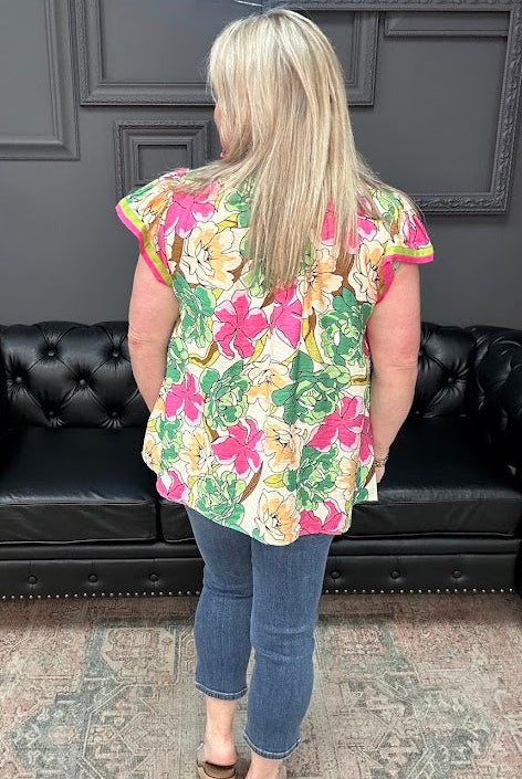 Person wearing a colorful floral top and blue jeans standing in front of a black leather couch.