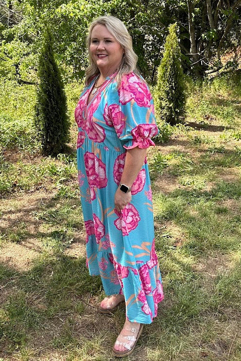 Woman in a blue and pink floral dress standing in a garden.
