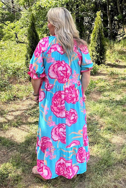 Woman wearing a blue and pink floral dress standing in a garden.