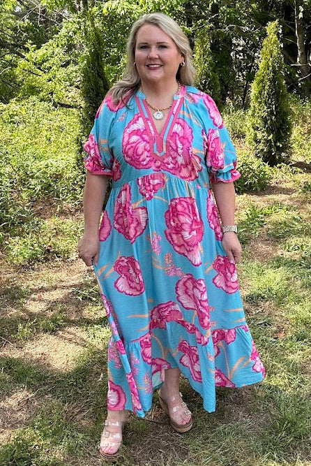Woman wearing a blue and pink floral dress standing in a garden.
