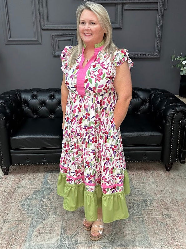 Woman wearing a floral dress with a pink top and green bottom in a room with black leather couches and gray walls.