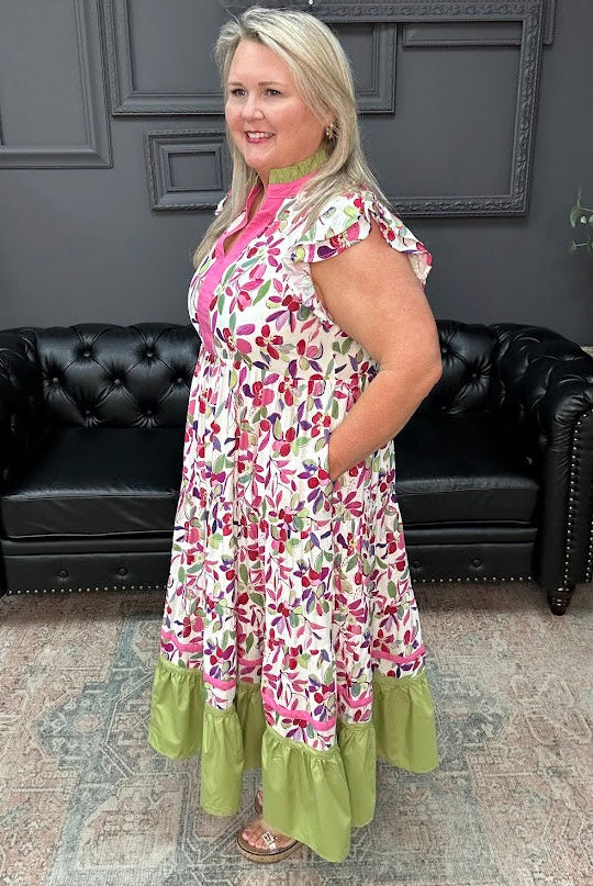 Woman wearing a floral dress with green ruffle hem in a room with black leather couches and gray walls.