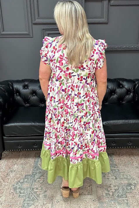 Woman wearing a floral dress with green hem in a room with black leather couches and gray walls.