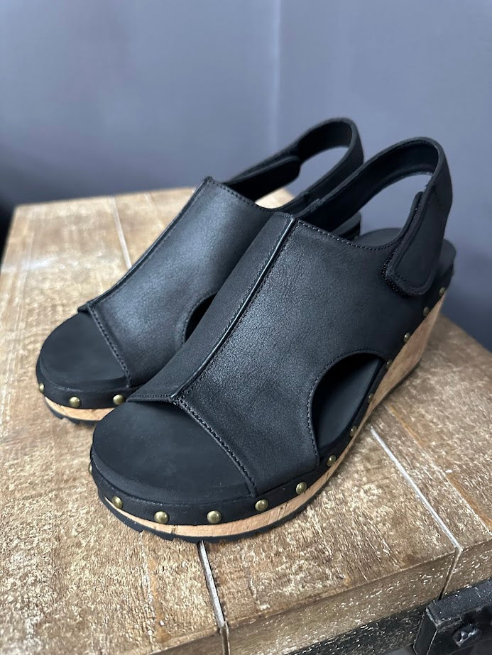 Black sandals with wooden sole on a textured surface