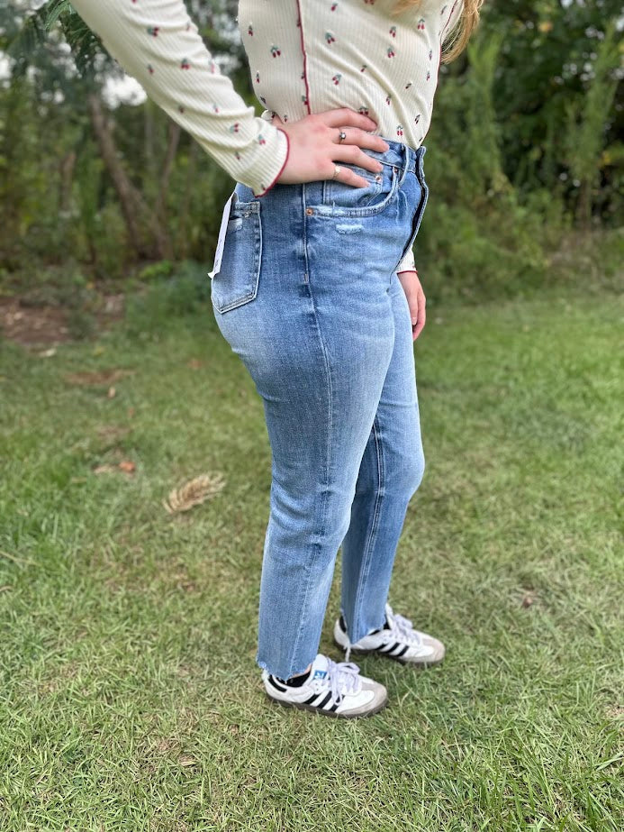 Person wearing light blue jeans and a cream top with floral patterns, standing outdoors on grass.