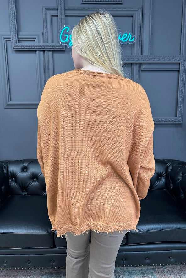 Person wearing a beige sweater in front of a dark blue wall with a neon sign.