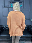 Person wearing a beige sweater in front of a dark blue wall with a neon sign.