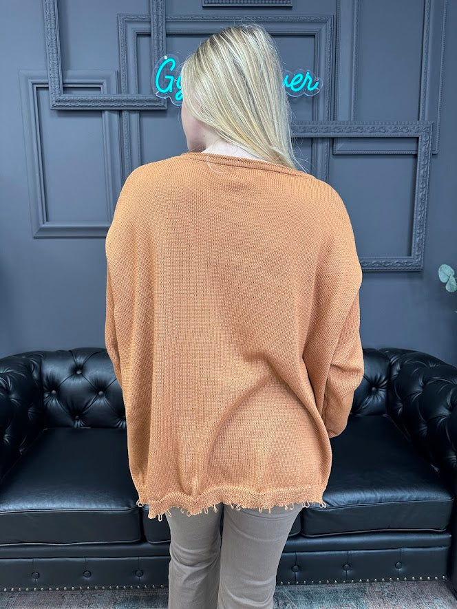 Person wearing a beige sweater in front of a dark blue wall with a neon sign.