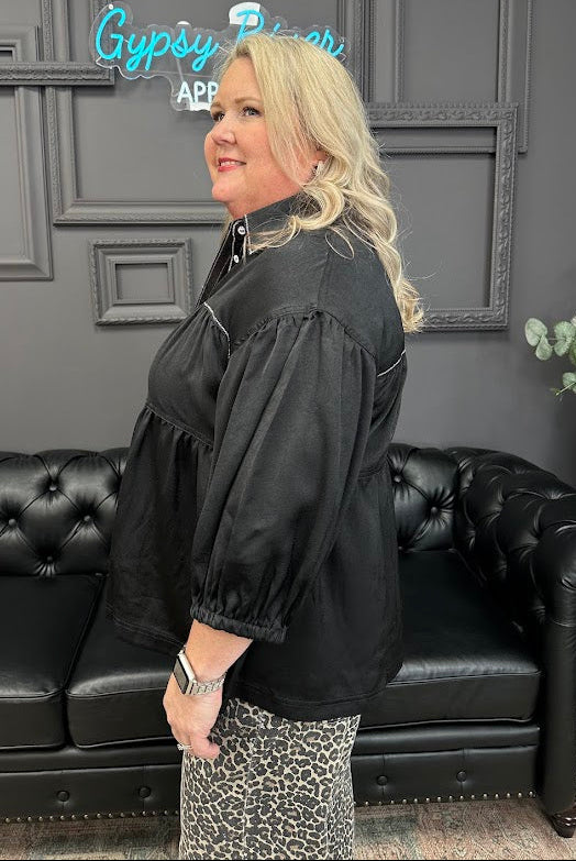 Woman in a black jacket standing in a room with a black couch and 'Gypsy Queen' sign.