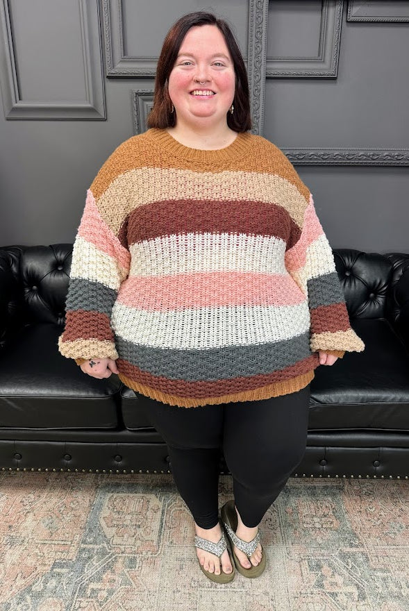 Person wearing a colorful striped sweater standing in a room with a black leather couch and gray walls.
