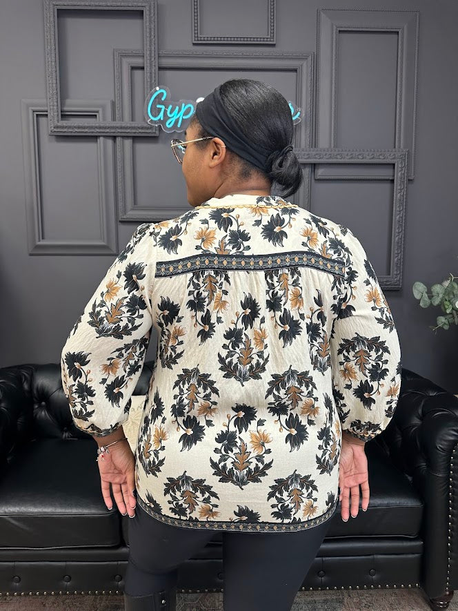 Person wearing a floral-patterned blouse in a room with a black couch and gray walls.