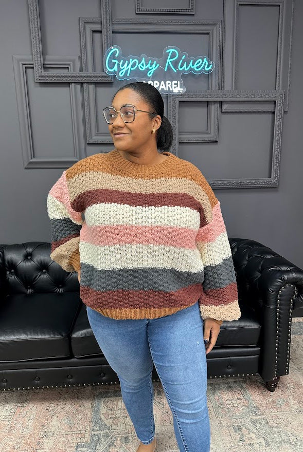 Woman wearing a striped sweater in a room with a black leather couch and gray walls.