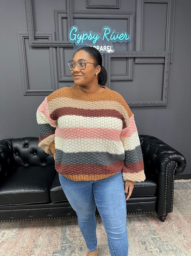 Woman wearing a striped sweater in a room with a black leather couch and gray walls.