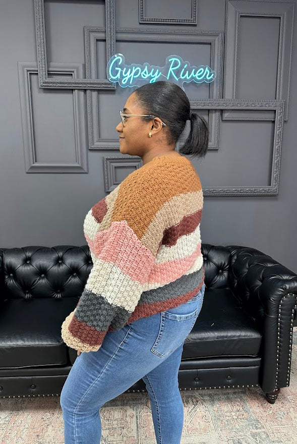 Person wearing a colorful knitted sweater standing in front of a black leather couch with a gray wall background.