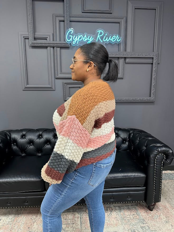 Person wearing a colorful knitted sweater standing in front of a black leather couch with a gray wall background.