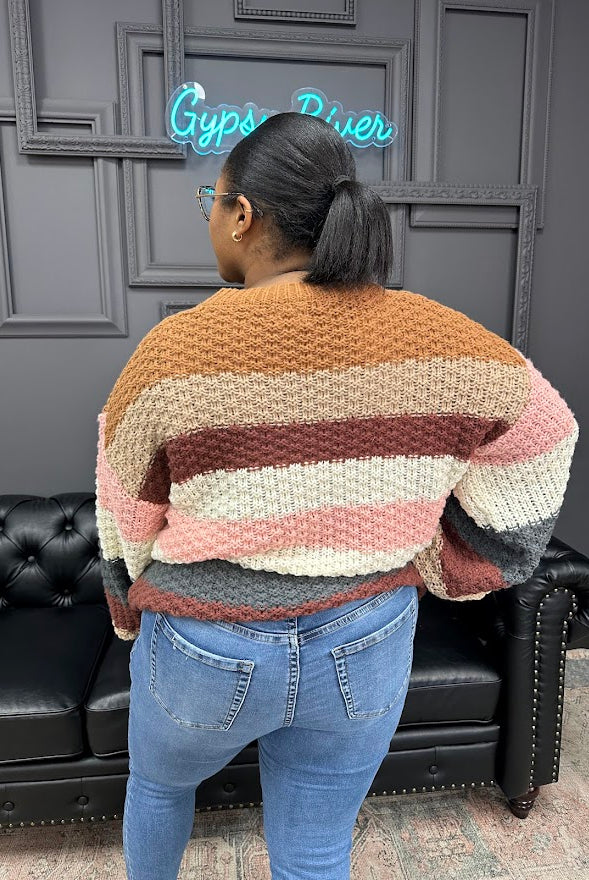 Person wearing a colorful striped sweater in front of a dark wall with a neon sign.