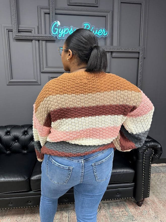 Person wearing a colorful striped sweater in front of a dark wall with a neon sign.