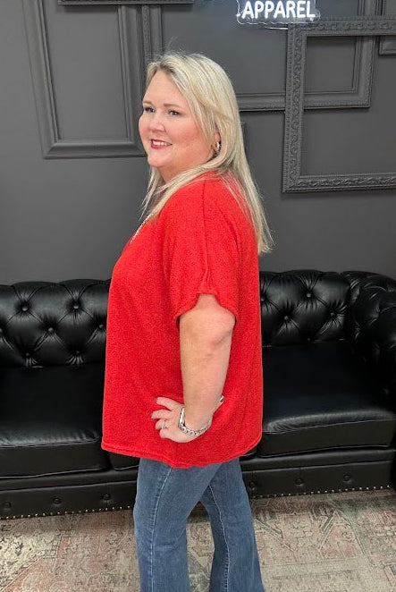 Woman in a red shirt and blue jeans standing in front of a black couch with a Christmas tree and 'Gypsy River Apparel' sign in the background.