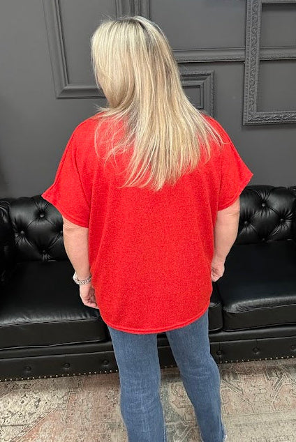 Person wearing a red shirt and blue jeans standing in front of a black leather couch with a Christmas tree and presents in the background.