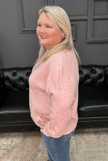 Woman in a pink sweater standing in front of a black leather couch with 'Gypsy River Apparel' branding.