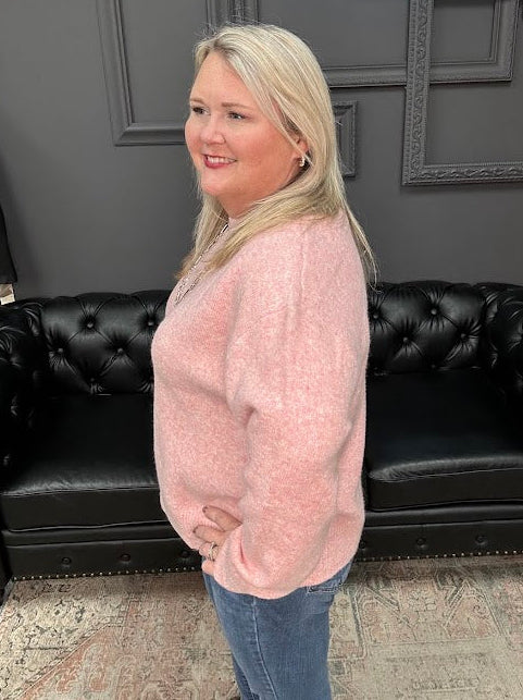 Woman in a pink sweater standing in front of a black leather couch with 'Gypsy River Apparel' branding.