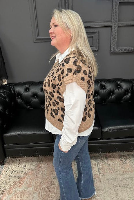 Woman wearing a leopard print vest and blue jeans standing in front of a black leather couch with 'Gypsy River Apparel' branding.