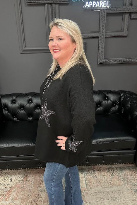 Woman in a black sweater with decorative elements standing in front of a black leather couch and 'Gypsy River Apparel' sign.