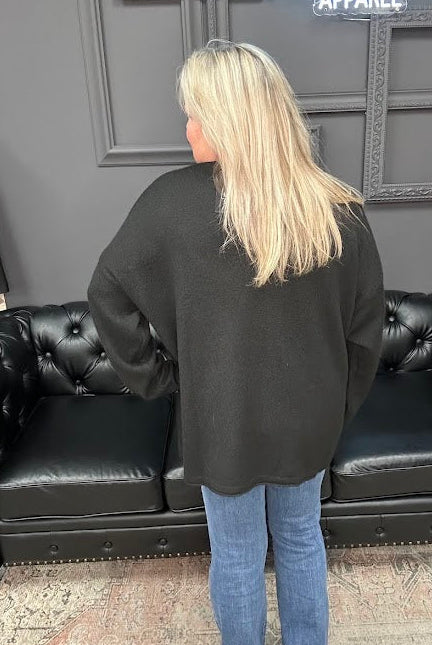Person wearing a black sweater and blue jeans standing in front of a black leather couch.
