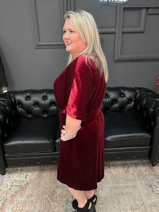 Woman in a burgundy dress standing in front of a black leather couch with 'Gypsy River Apparel' branding.