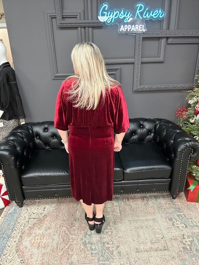 Person wearing a red velvet dress standing in front of a black leather couch with 'Gypsy River Apparel' branding.