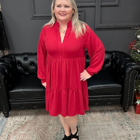 Woman in a red dress standing in front of a black couch and Christmas tree with 'Gypsy River Apparel' sign.