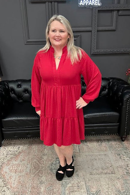 Woman in a red dress standing in front of a black couch and Christmas tree with 'Gypsy River Apparel' sign.