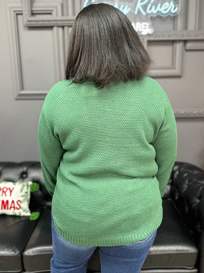 Person wearing a green sweater in a room with a black couch and decorative pillows.