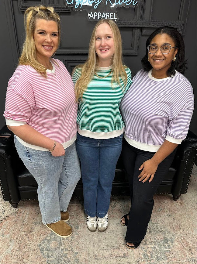 Three women posing together in a store setting with a sign in the background.